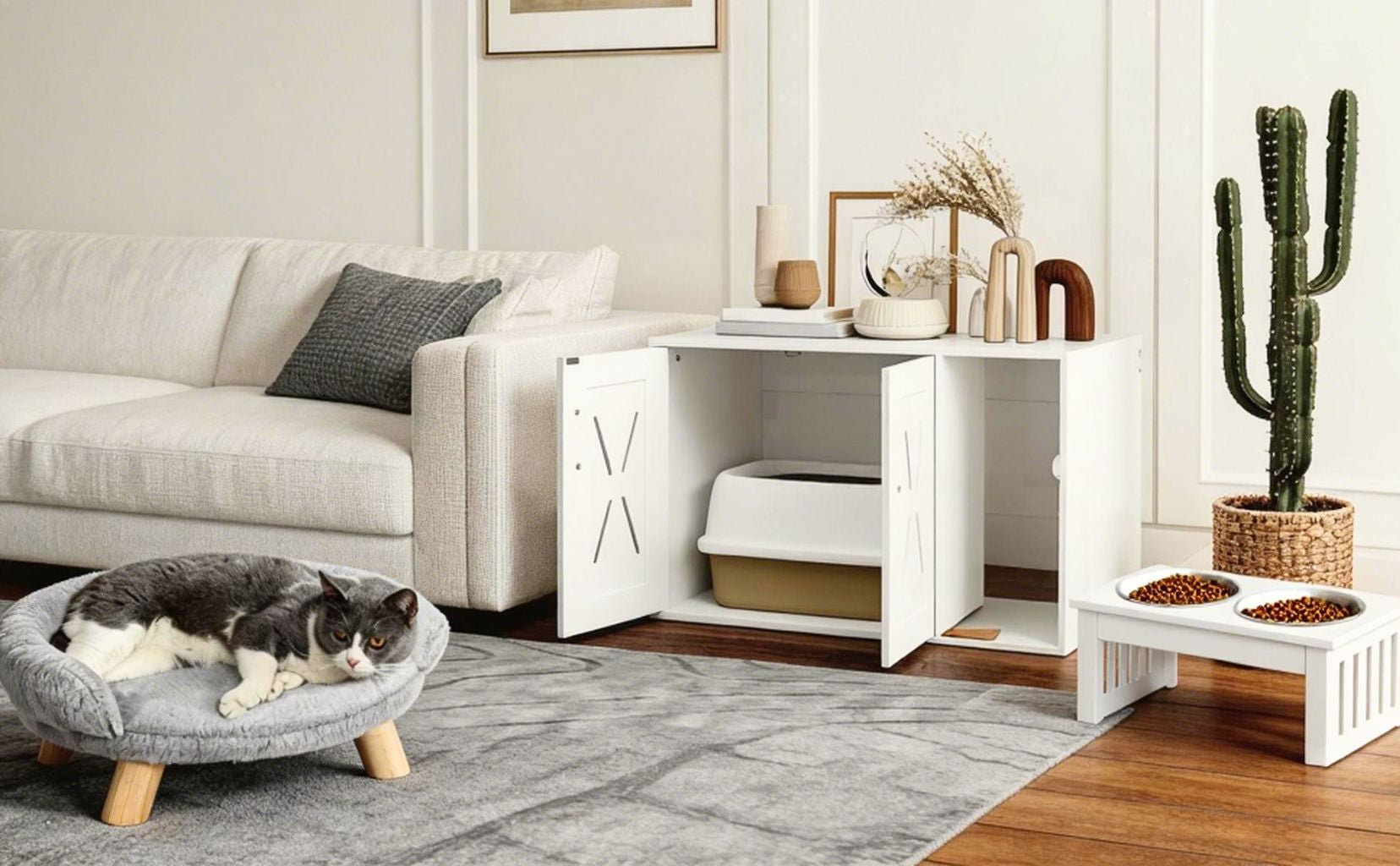 Living room with a cat on a small ottoman, a white pet bed, and a cactus plant.